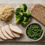 Stone cutting board with cooked brown rice, fresh broccoli florets, whole grain bread, sliced roasted turkey breast, and a bowl of green beans