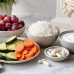 Low FODMAP foods including rice, carrots, zucchini, and grapes beside probiotic capsules and plain yogurt on a light counter